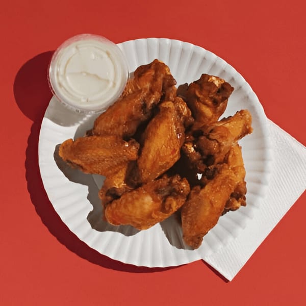 Joey's Pizza chicken wings on a white paper plate with a side of ranch dressing.