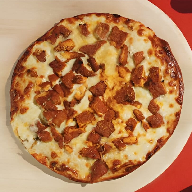 A round, cheesy pizza with crispy brown chicken pieces on a white plate, from Joey's Pizza.