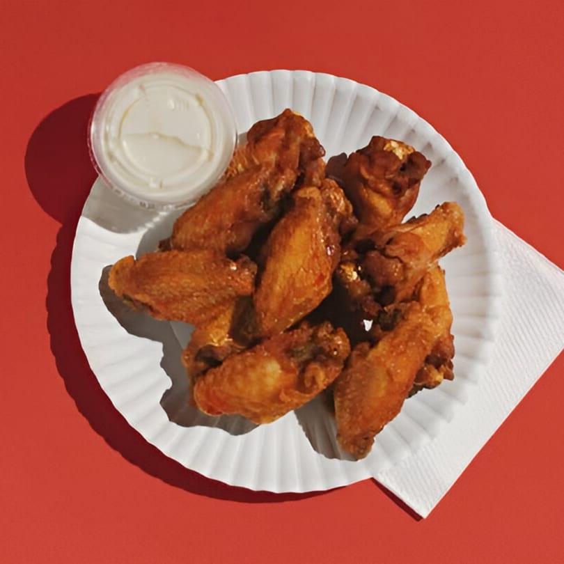 Golden-brown chicken wings and a container of dipping sauce on a white paper plate.