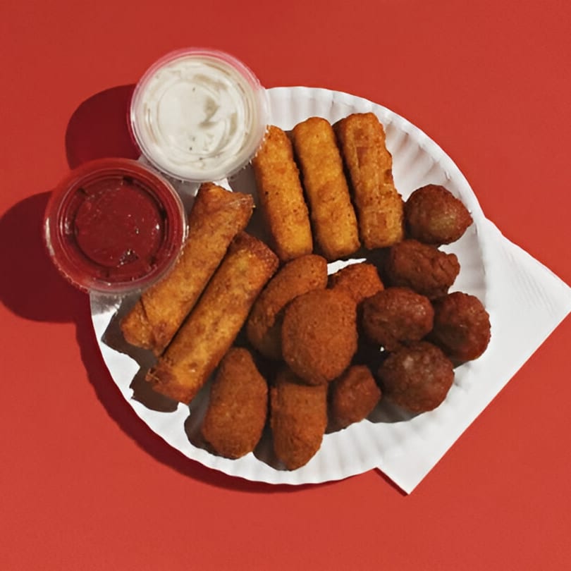 A white paper plate filled with fried appetizers and two dipping sauces on a red background.