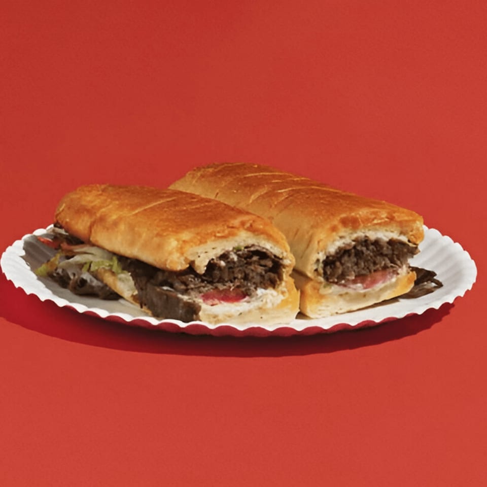 Two steak and cheese subs with lettuce and tomato on a white paper plate.