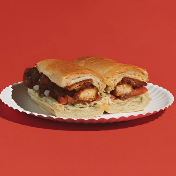 Two chicken parmesan subs with red sauce and cheese on a white paper plate against a red background.