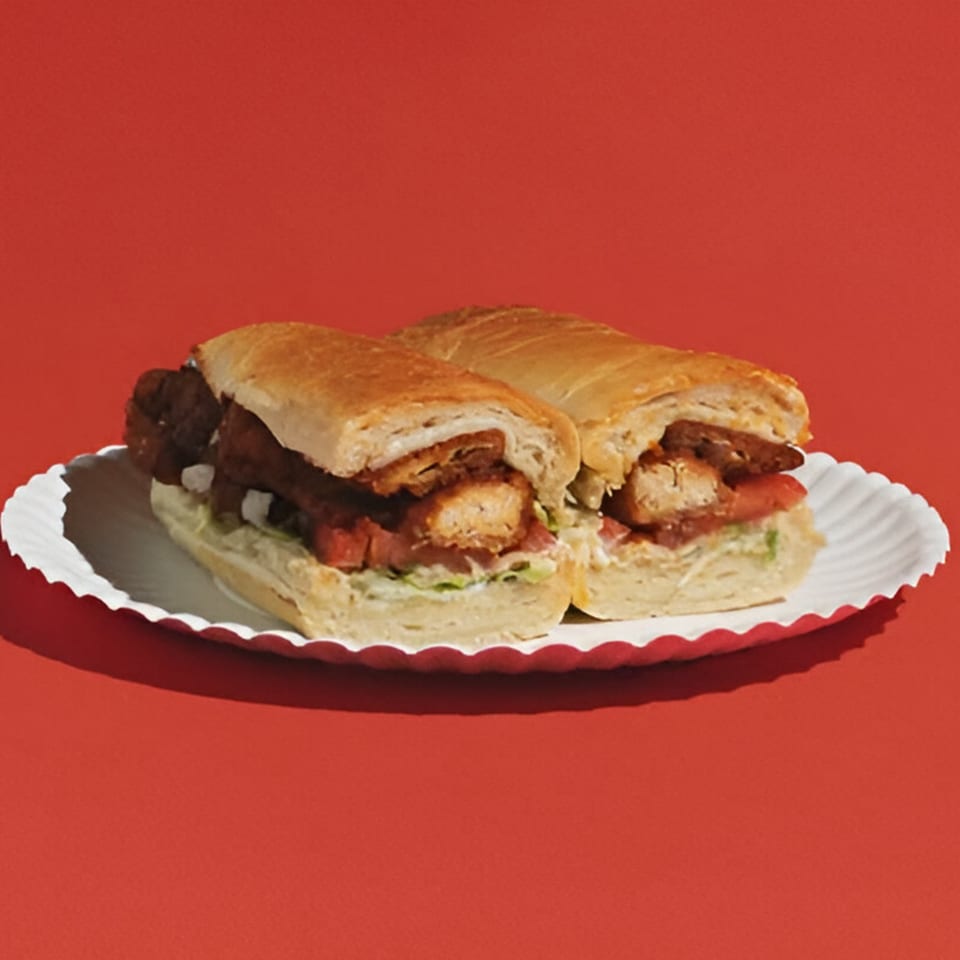 Two chicken parmesan subs on a white paper plate against a vibrant red background.