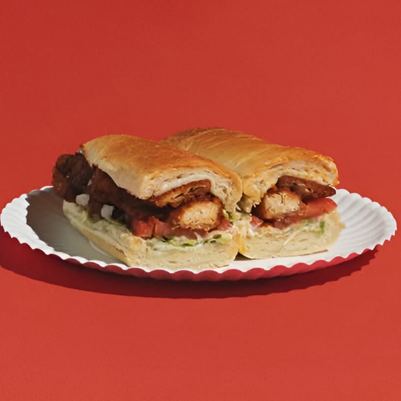 Two chicken parmesan subs on a white paper plate against a vibrant red background.