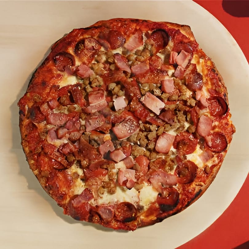 A whole Joey's Pizza with pepperoni, ham, and sausage on a light plate.